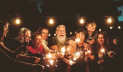 Happy family celebrating with sparklers fireworks at night party - Group of people with different ages and ethnicity having fun together - Holidays lifestyle concept