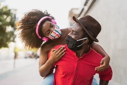 African couple piggyback wearing face mask - Happy Afro people having fun outdoor - Health care and youth relationship concept 