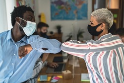 Young multiracial workers wearing face mask doing new social distance greetings bumping elbows inside co-working creative space - Focus on male hand