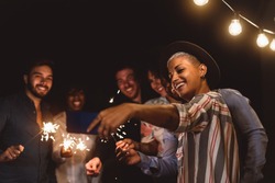 Happy young friends celebrating new year eve with sparklers fireworks while taking selfie with mobile smartphone on patio house party - Youth people lifestyle and holidays concept