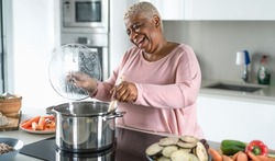Happy senior woman having fun preparing lunch in modern kitchen - Hispanic Mother cooking for the family at home