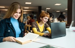 Young university students using laptop and reading book in library - School education concept
