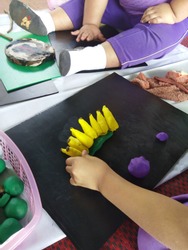 Children are molding banana plasticine clay on black flute board. 
