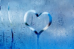 Hand draw a heart and drops of water on the glass. Condensation and raindrops on the window, shallow depth of field
