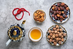 Popular food during Iftar  - macadamia nuts, pistachios, walnuts, dry dates. Karan, rosary, teapot, bowl with black tea on concrete background Top view Flat lay Muslim holiday of holy month of Ramadan