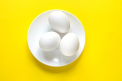 Three white eggs on a round plate lie on a colorful yellow background. Good morning concept