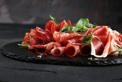 Marble cutting board with prosciutto, bacon, salami and sausages on wooden background. Meat platter appetizers 