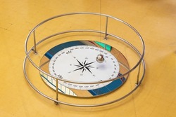 Long exposure photography  of a Foucault pendulum swinging on a compass rose. The pendulum is blurred by movement