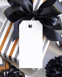 Present with vertical blank gift tag and black bow close up. Gift boxes wrapped in Striped geometric paper near black and white decor. Christmas, New Year, Birthday, Anniversary label mockup