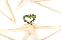 Conscious consumption slow fashion concept. Heart of clothes hangers entwined with green plant on white background. Sustainable eco lifestyle. Top view flat lay
