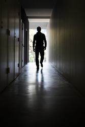 Man walking down a dark corridor towards a well lit end/exit