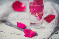 Rose pink water - water with petals of rose flowers in a transparent glass