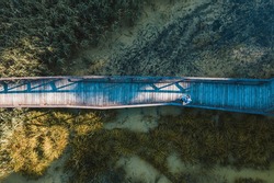 Aerial top view of wooden bridge pathway over marshy river, summer travel concept.