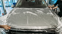 Process of armoring car hood with transparent polyurethane anti-gravel film cover coating in car detailing studio garage