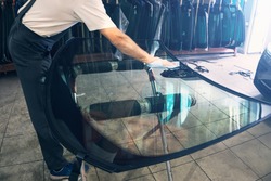 Automobile glazier worker degreases glass windscreen or windshield before installation on car in service station garage