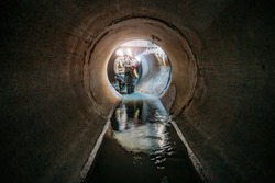 Sewer tunnel workers examines sewer system damage and wastewater leakage