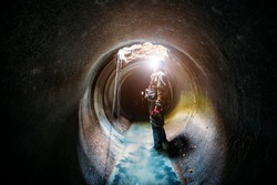 Sewer tunnel worker examines sewer system damage and wastewater leakage.