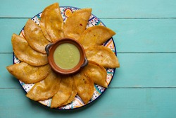 Traditional mexican basket tacos also called canasta with  green sauce on turquoise background