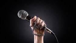World press freedom day concept. Hand holding a microphone with chain on dark background, symbol of press freedom or speech freedom.