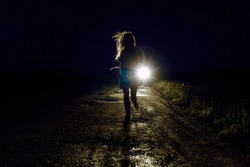 running female silhouette on a night country road running away from pursuers by car in the light of headlights