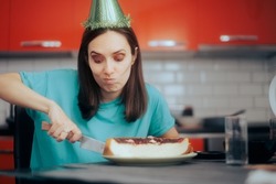 Stressed Birthday Girl Cutting a Homemade Cheesecake. Upset woman enjoying her birthday cake alone in the kitchen
