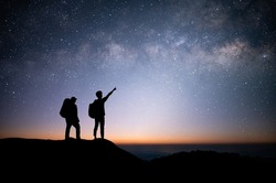 Silhouette of young couple traveler and backpacker standing and watched the star and milky way on top of the mountain. He enjoyed traveling and was successful when he reached the summit.