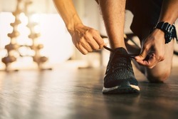 A male athlete tying his shoelaces at the gym in the morning. He usually comes to exercise every morning in the morning. Exercise keeps him energized and keeps him healthy.