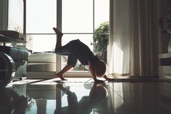 Little yogi child is practicing yoga indoors. Preschool years old boy meditating and doing the yoga poses at home. Beautiful photo of silhouette of cute child in Downward-Facing Dog pose.
