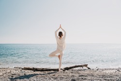 Yoga on the beach. Woman practicing yoga on coastline of the ocean. Beautiful girl relaxing by the sea. Calm, serene, minimalist photo with copy space. Healthy active lifestyle, vitality, zen.