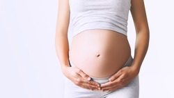 Pregnant woman holds hands on her belly on white background, close-up. Beautiful photo of pregnancy. Mother waiting for baby. Women prepare for maternity. Concept of prenatal period, maternal health.
