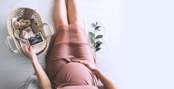 Pregnant woman in dress with ultrasound image. Mother with wicker basket of cute tiny stuff and teddy bear toy for newborn. Expectant mother waiting and preparing for baby birth during pregnancy.