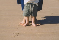 Baby's first steps. Mother and small child walking barefoot on beach sand near by ocean. Happy young family in nature. Mother and baby playing outdoors on sea beach. Close-up human feet.