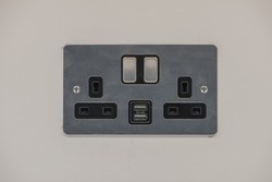 UK brushed chrome double socket with USB port on a wall. Close up view.