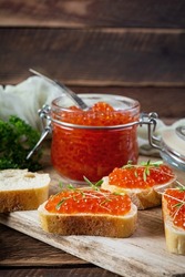 Delicious fresh red caviar with baguette toasts on wooden background