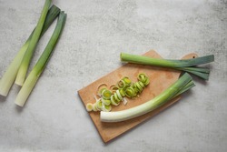 Freshly harvested leeks on a wooden chopping board  on a stone background with some leek rings slices chopped. Top view, copy space
