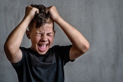Teen boy screaming in anger on dark background 