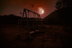 Night photo of metal swing standing outdoor at night with Moon. Nobody there. Lonelyness concept