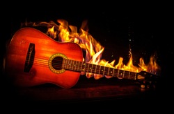 Music concept. Acoustic guitar on a dark background under beam of light with smoke with copy space. Exploding guitar. Fire effects. Surreal guitar. Selective focus