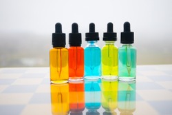 Vape concept. Beautiful colorful vape liquid glass bottles outdoor on chessboard. Useful as background or electronic cigarette advertisement. Selective focus