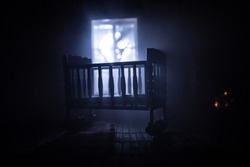 Old creepy eerie baby crib near window in dark room. Scary baby silhouette in dark. A realistic dollhouse living room with furniture and window at night. Selective focus