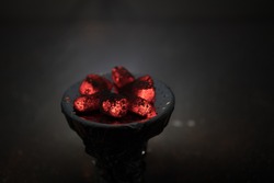 Close-up of burning charcoal cubes. Action. Cubes of embers burning in bowl for smoking hookah. Creative artwork decoration on dark background. Empty space. Selective focus