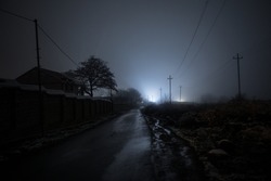 Night street country road with buildings and fences covered in fog lamp . Or Mysterious night in Azerbaijan mountain village. Long exposure shot