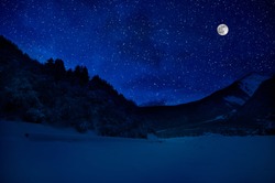 Mountain Road through the snowy forest on a full moon night. Scenic night winter landscape of dark blue sky with moon and stars. Azerbaijan