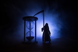 Time concept. Scary view of grim reaper silhouette standing at hourglass with smoke and lights on a dark background. Surreal decorated picture