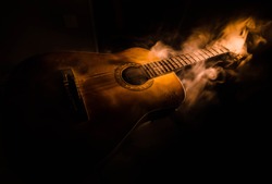 Music concept. Acoustic guitar isolated on a dark background under beam of light with smoke with copy space. Guitar Strings, close up. Selective focus. Fire effects. Surreal guitar