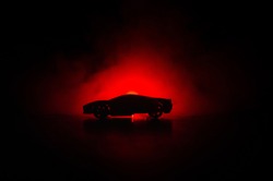 The car in the shadows with glowing lights in low light, or silhouette of sport car dark background. Selective focus