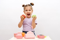 concept of healthy and unhealthy food, little smiling blonde girl in purple T-shirt chooses between green apple and hamburger, children's game in store at home concept, plastic toy food