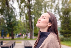 Portrait of young beautiful woman doing breath of fresh autumn air in a green Park. the concept of pure atmospheric air