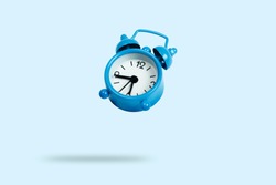 Flying blue alarm clock on a blue background. Levitation
