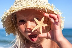 Cheerful child girl in panama holding a starfish on the beach 